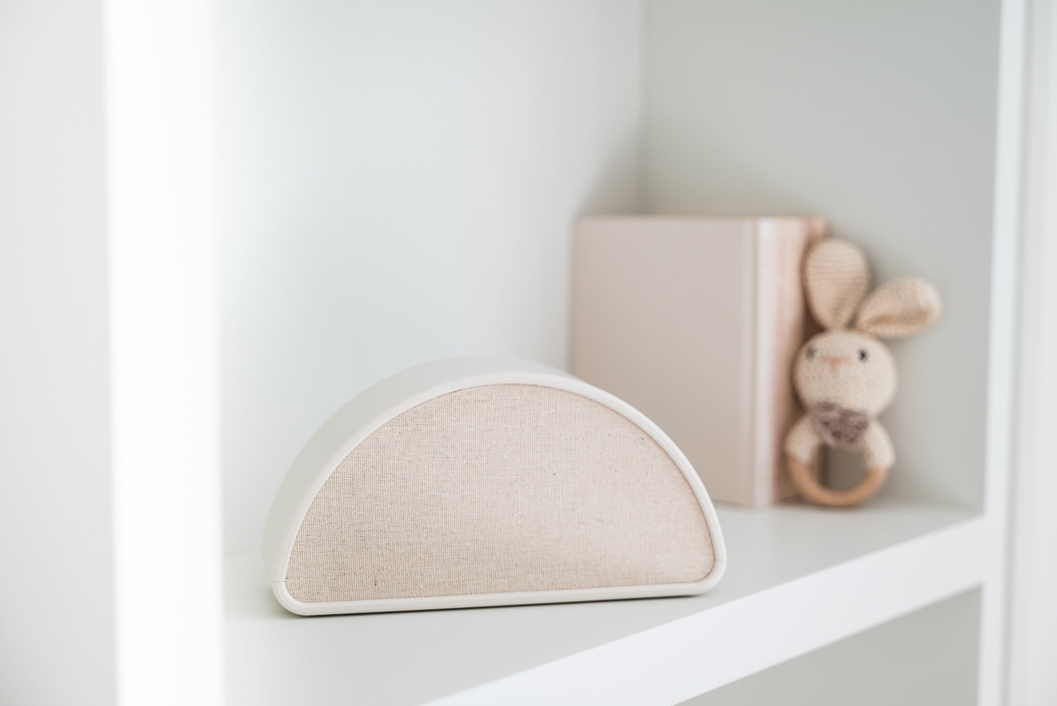 Shushiie, the dreamy baby sleep speaker, on a nursery shelf next to baby books and a bunny rattle