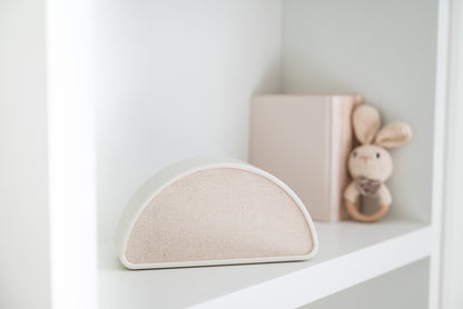 Shushiie, the dreamy baby sleep speaker, on a nursery shelf next to baby books and a bunny rattle